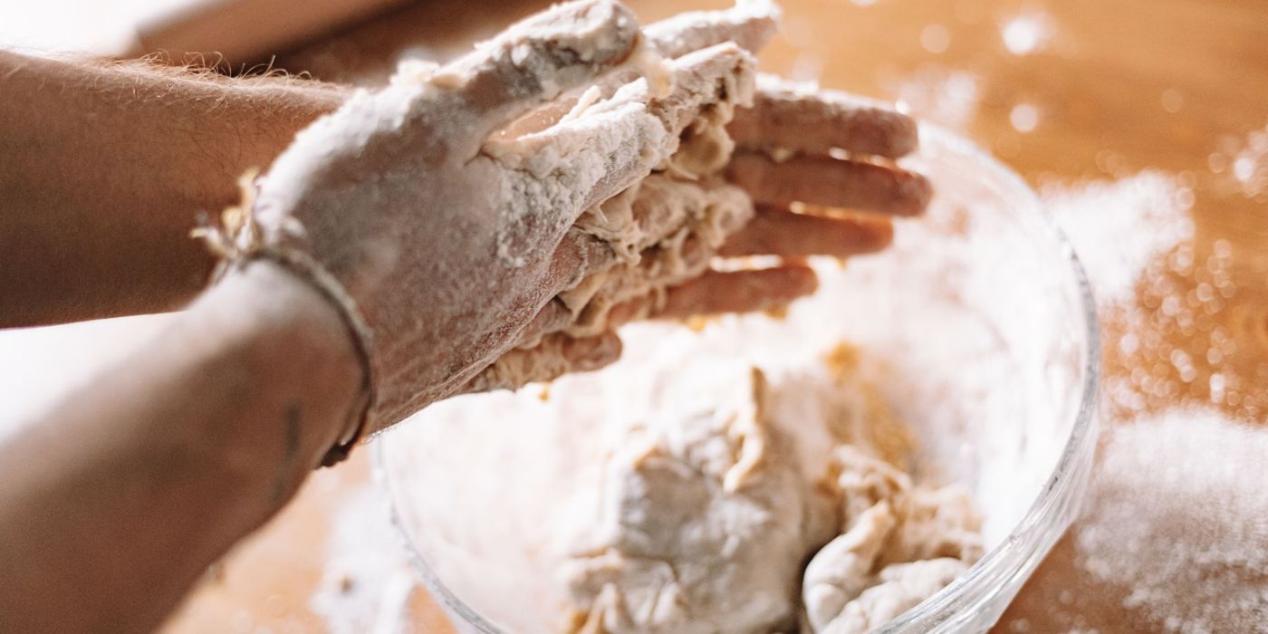 Tangan menyediakan doh roti dengan tepung di atas meja bakeri